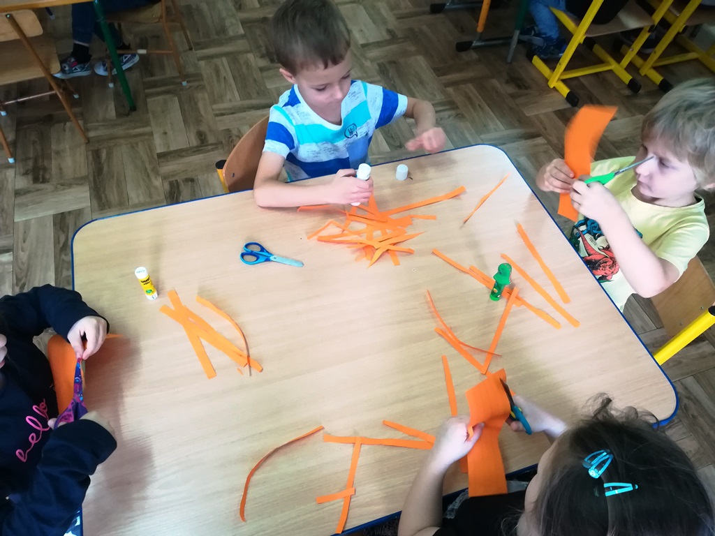 dzieci wycinają nożyczkami pomarańczowe paski 
