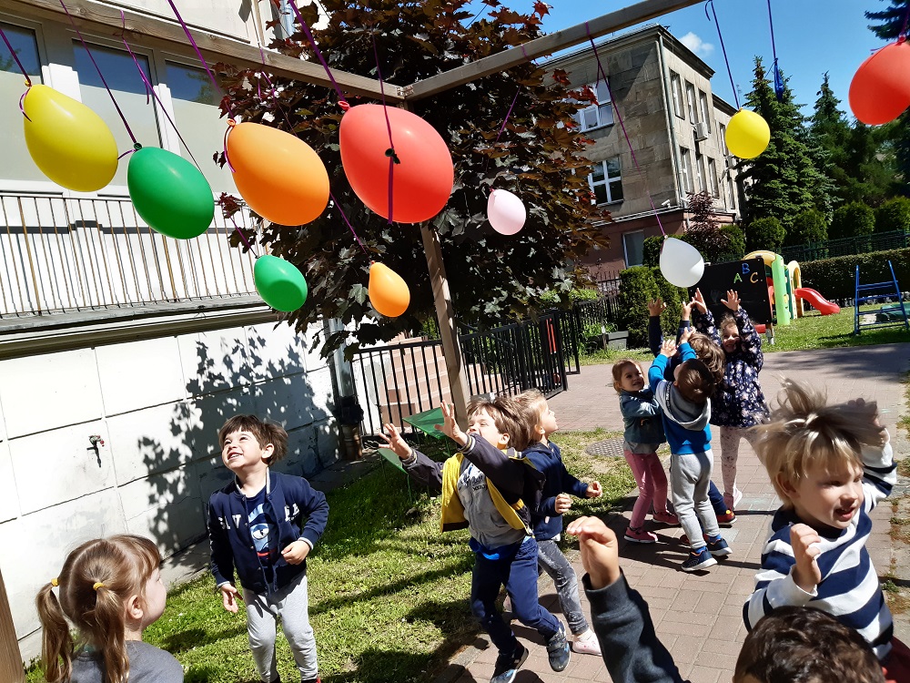dzieci podskakują do zawieszonych na nitkach balonów