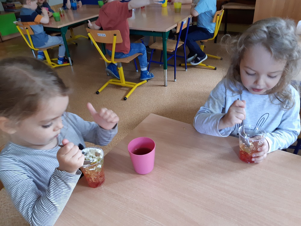 dzieci z apetytem jedzą deser - galaretkę z bitą śmietaną