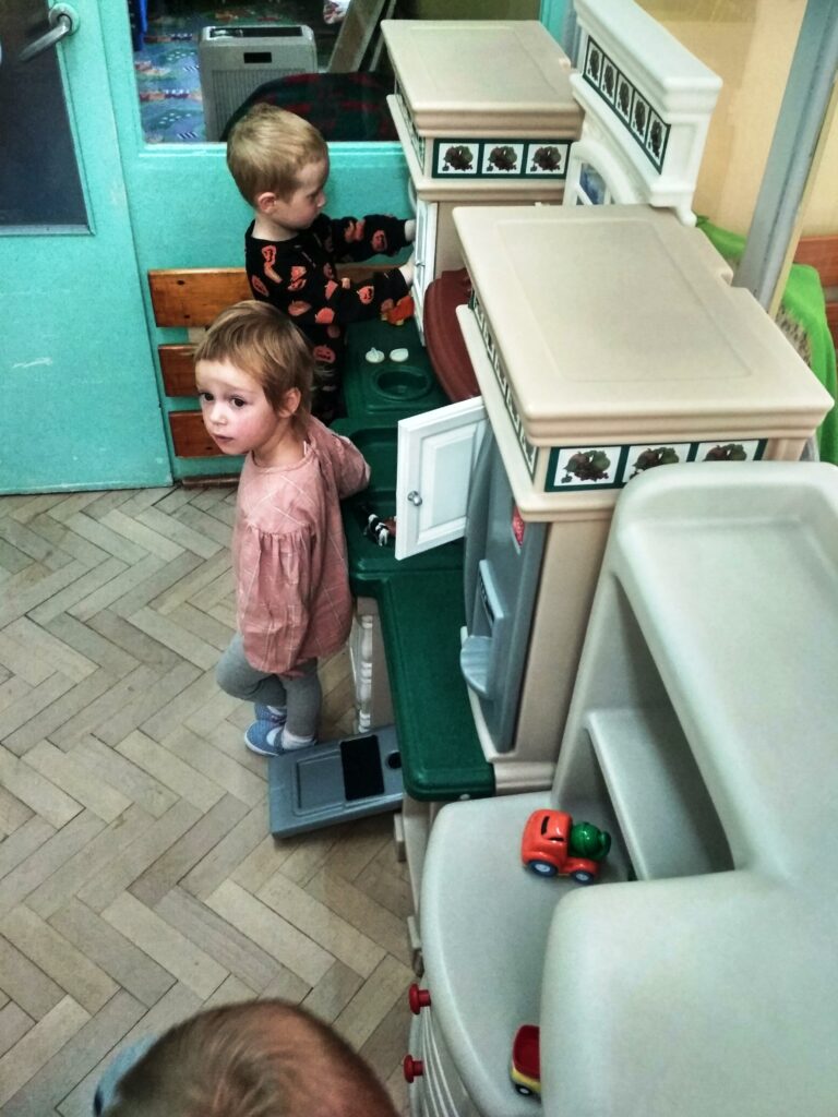 dziewczynka i chłopiec bawią się w kąciku kuchennym