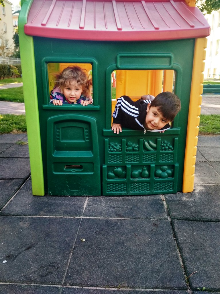 Dziewczynka i chłopiec bawią się w domku, wyglądają przez okna