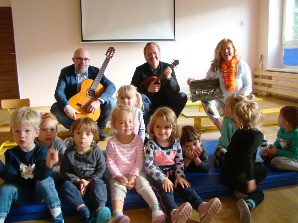 wspólne zdjęcie grupy dzieci z artystami -  dwaj panowie z gitarami i pani wokalistka