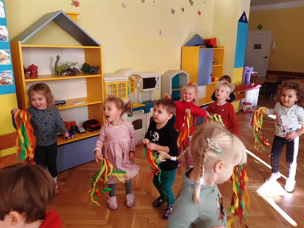  roześmiane dzieci tańczą wymachując paskami krepiny w jesiennych kolorach