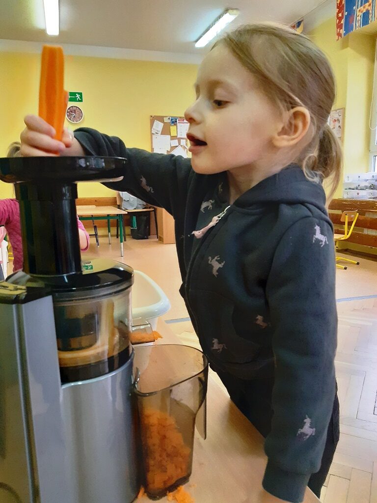 dziewczynka z wielkim przejęciem wkłada marchewkę do sokowirówki