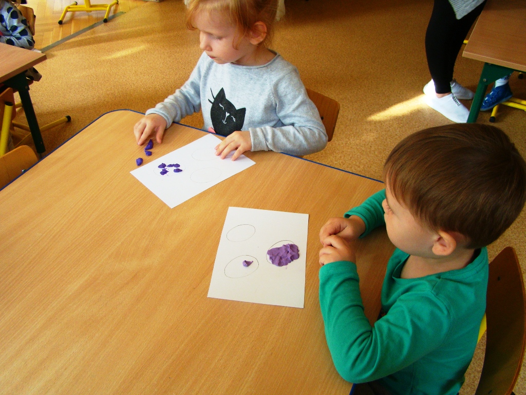 chłopiec i dziewczynka wylepiają fioletową plasteliną kontury śliwek na kartce