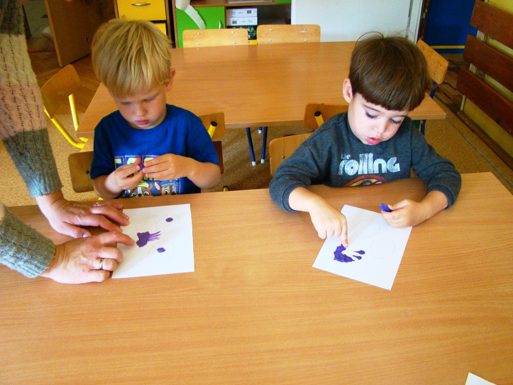 chłopcy wylepiają fioletową plasteliną kontury śliwek na kartce
