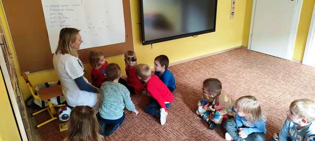 Dzieci siedzą na dywanie, dziewczynka oglądają model oka